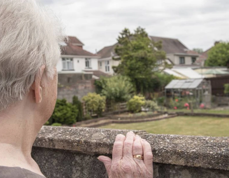 Personne âgée qui observe un jardin par dessus un muret